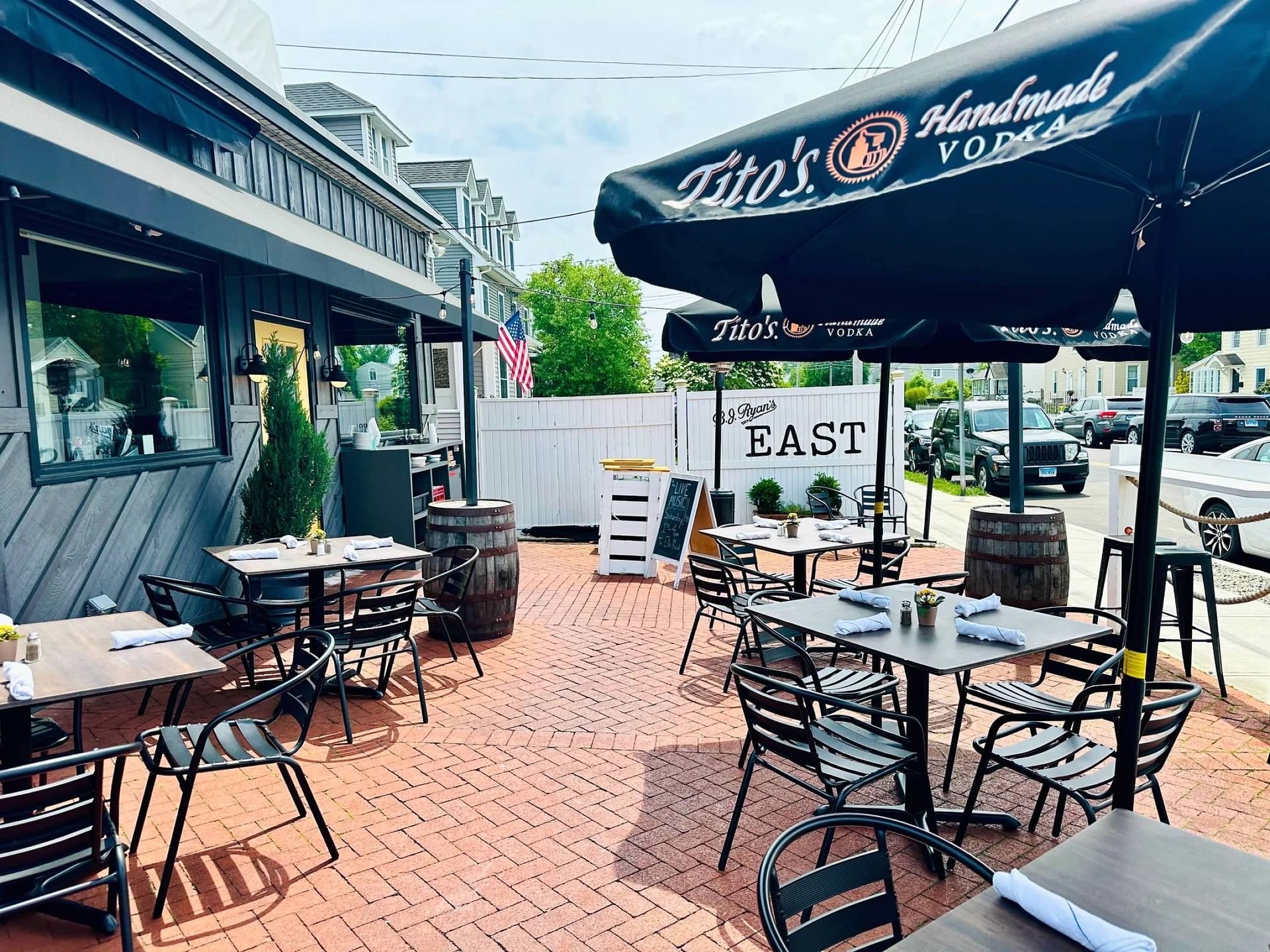 Outdoor dining patio with tables and chairs under Tito's Vodka branded umbrellas, set on a red brick ground.