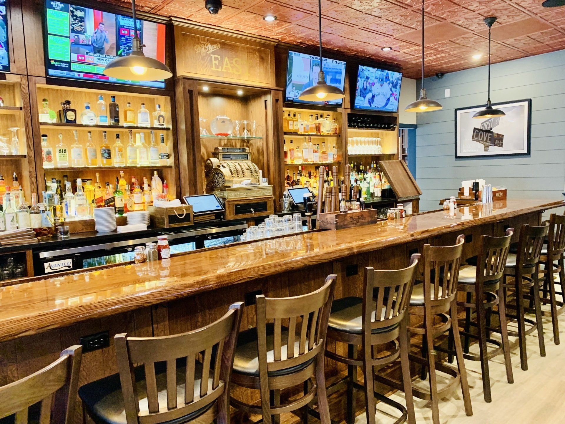 Empty wooden bar with stools and illuminated liquor shelves under a patterned ceiling.