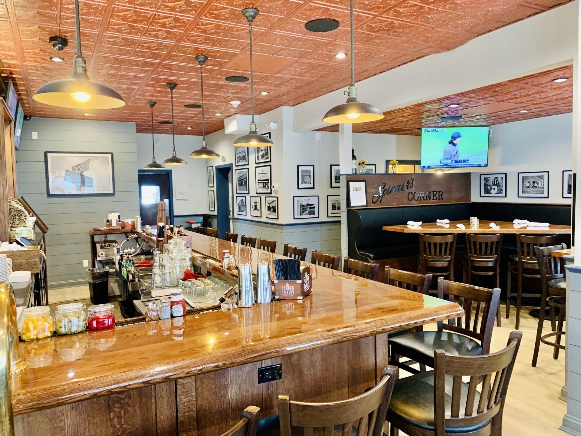 An interior shot of a restaurant featuring a long wooden bar with stools and a copper-colored tin ceiling.