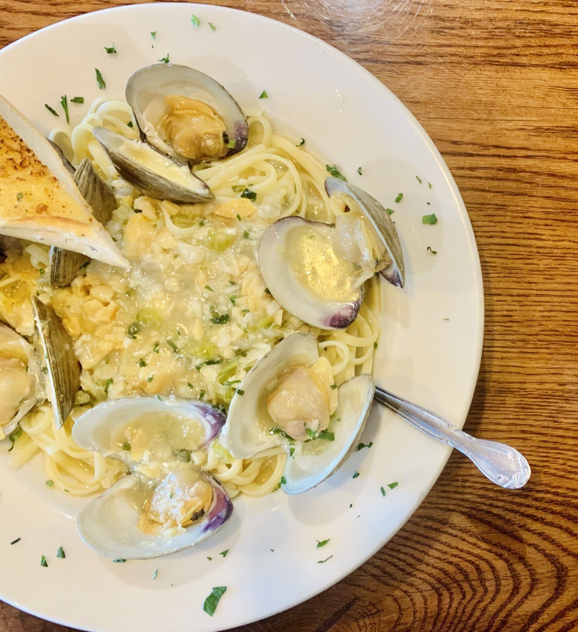 A plate of linguine with clams in a creamy sauce, garnished with parsley and served with a slice of toasted bread.
