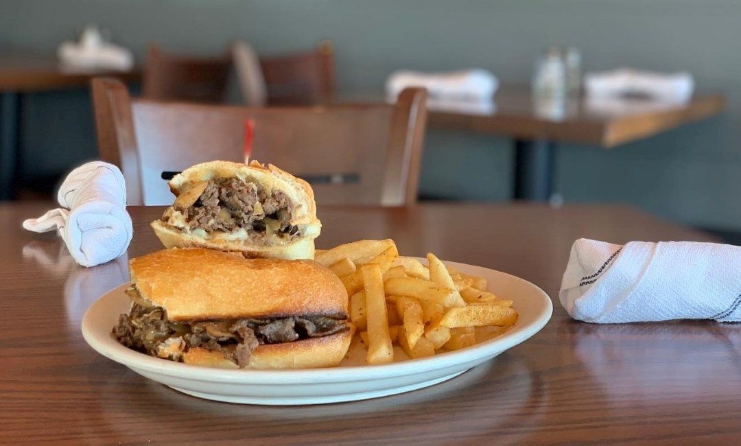 A steak sandwich with fries served on a white plate in a restaurant setting.