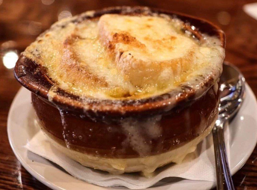A single serving of French onion soup in a brown ceramic crock, topped with melted cheese and a toasted bread slice.