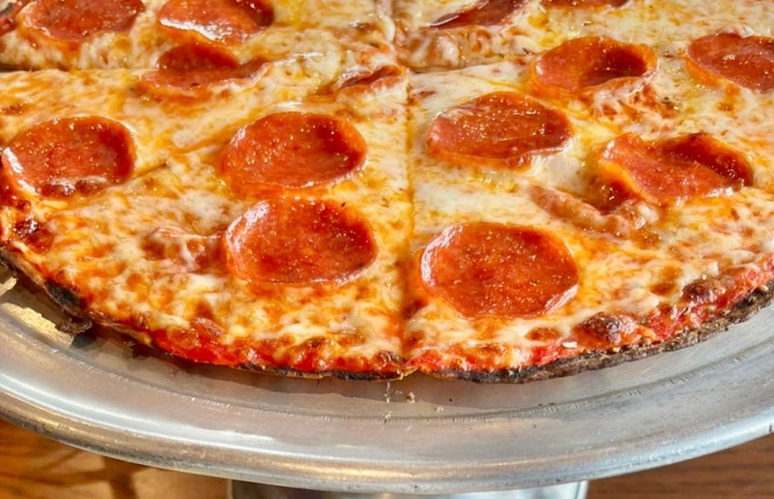A close-up shot of a round pepperoni pizza with melted cheese and red pepperoni slices on a metallic serving tray.