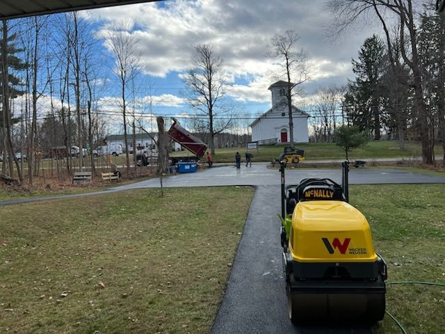 Yellow construction vehicle on a park path near a church and playground on a cloudy day