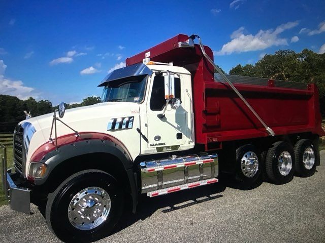 White and red dump truck parked on a road under a blue sky