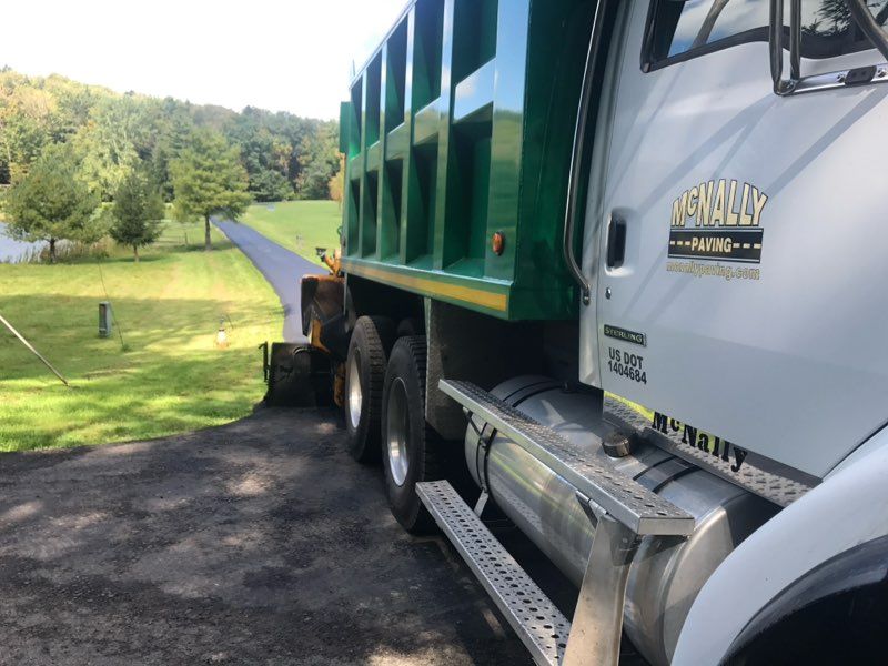 White dump truck parked on a gravel driveway beside a green lawn and trees in a rural area