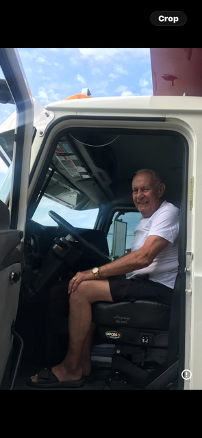 Person smiling in the driver’s seat of a white truck with the door open, holding a phone.