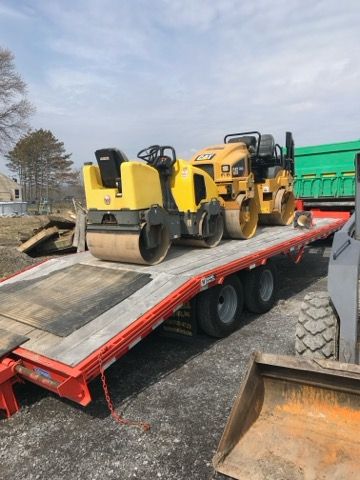 Yellow road rollers on a red trailer at a construction site, with a dump truck nearby.
