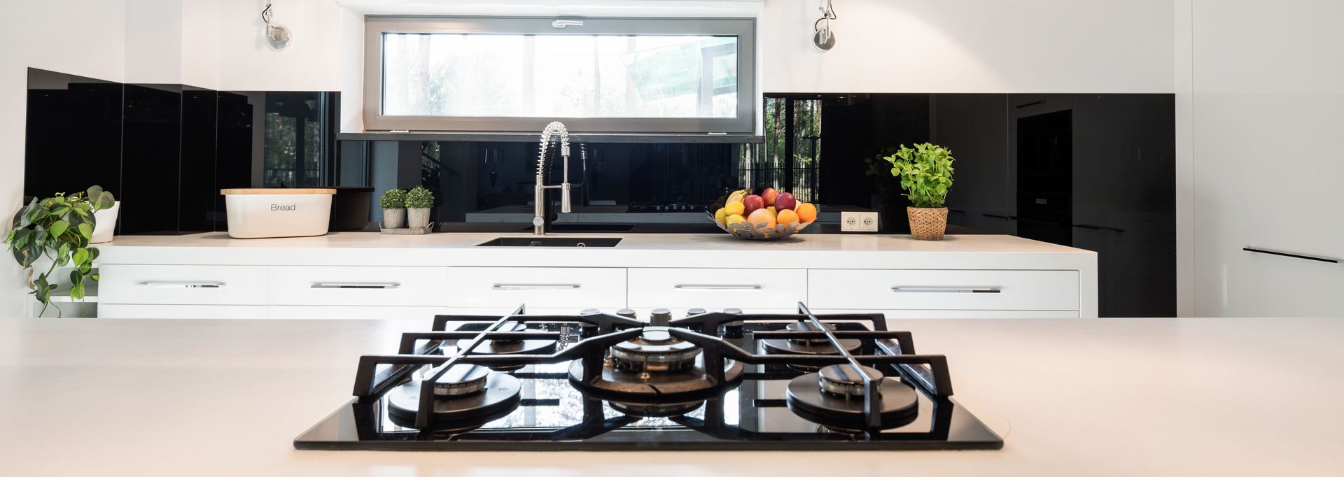 Modern kitchen with a sleek white countertop and black splashback and a gas stove in the foreground. Modern kitchen with a sleek white countertop and black splashback and a gas stove in the foreground.
