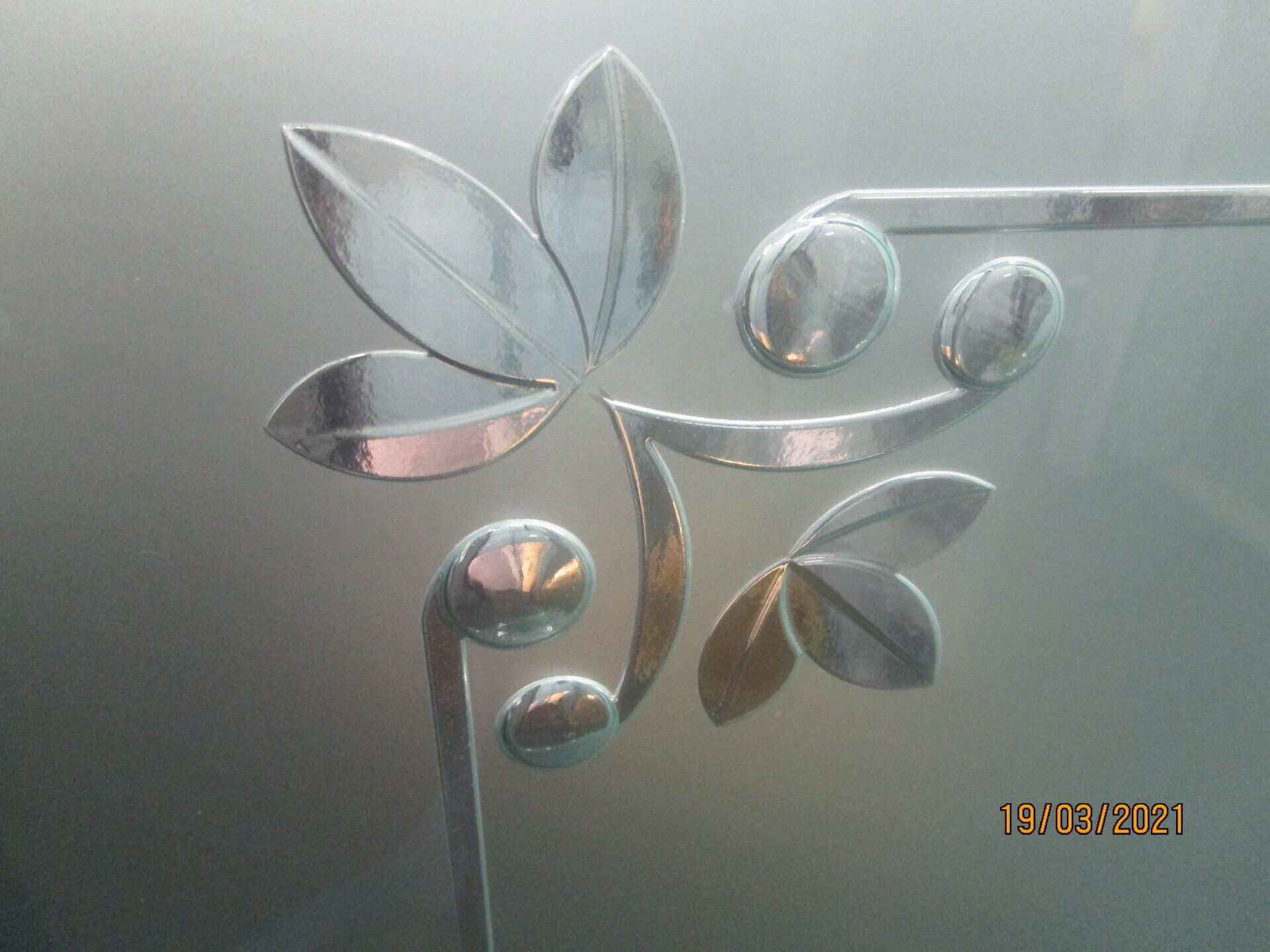 Silver floral wall decal on a frosted glass surface with a small gold date stamp.