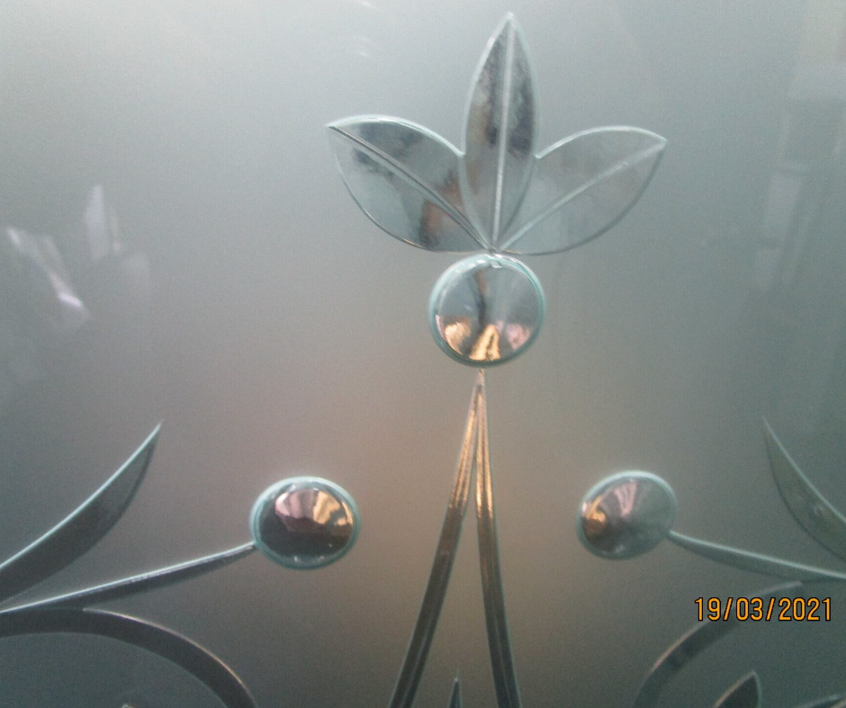 Frosted glass panel with etched leaf and circular floral design on a gray background.