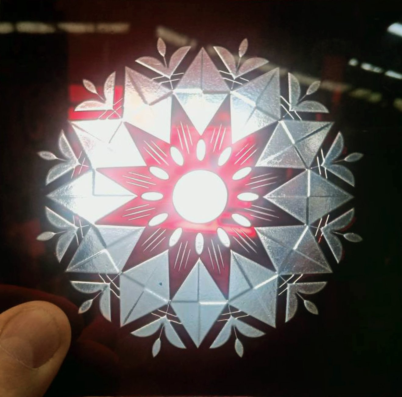 Hand holding a translucent geometric star ornament with a red center and silver-white faceted pattern