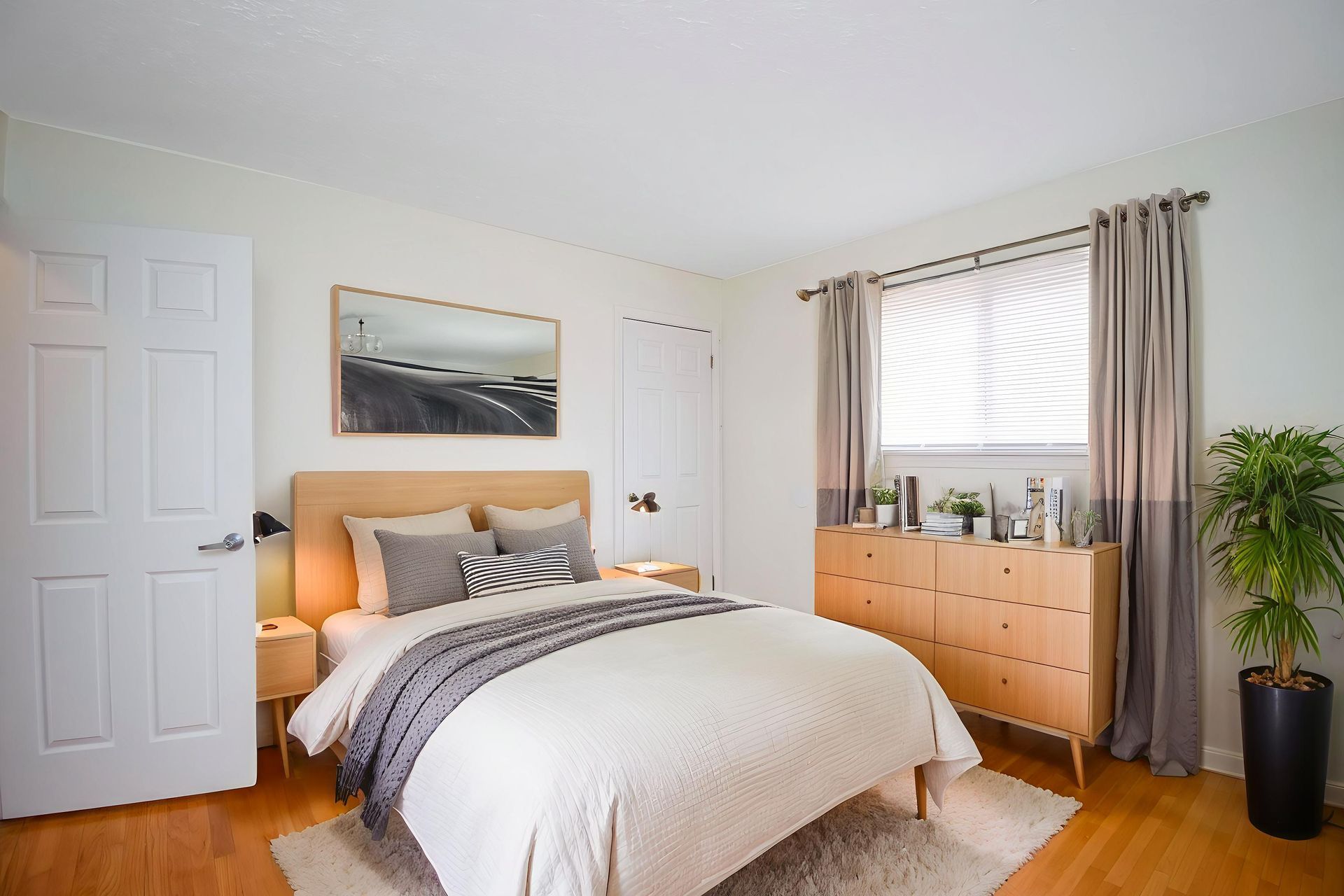 Bright bedroom with a bed, dresser, window, and beige curtains on a light wood floor.