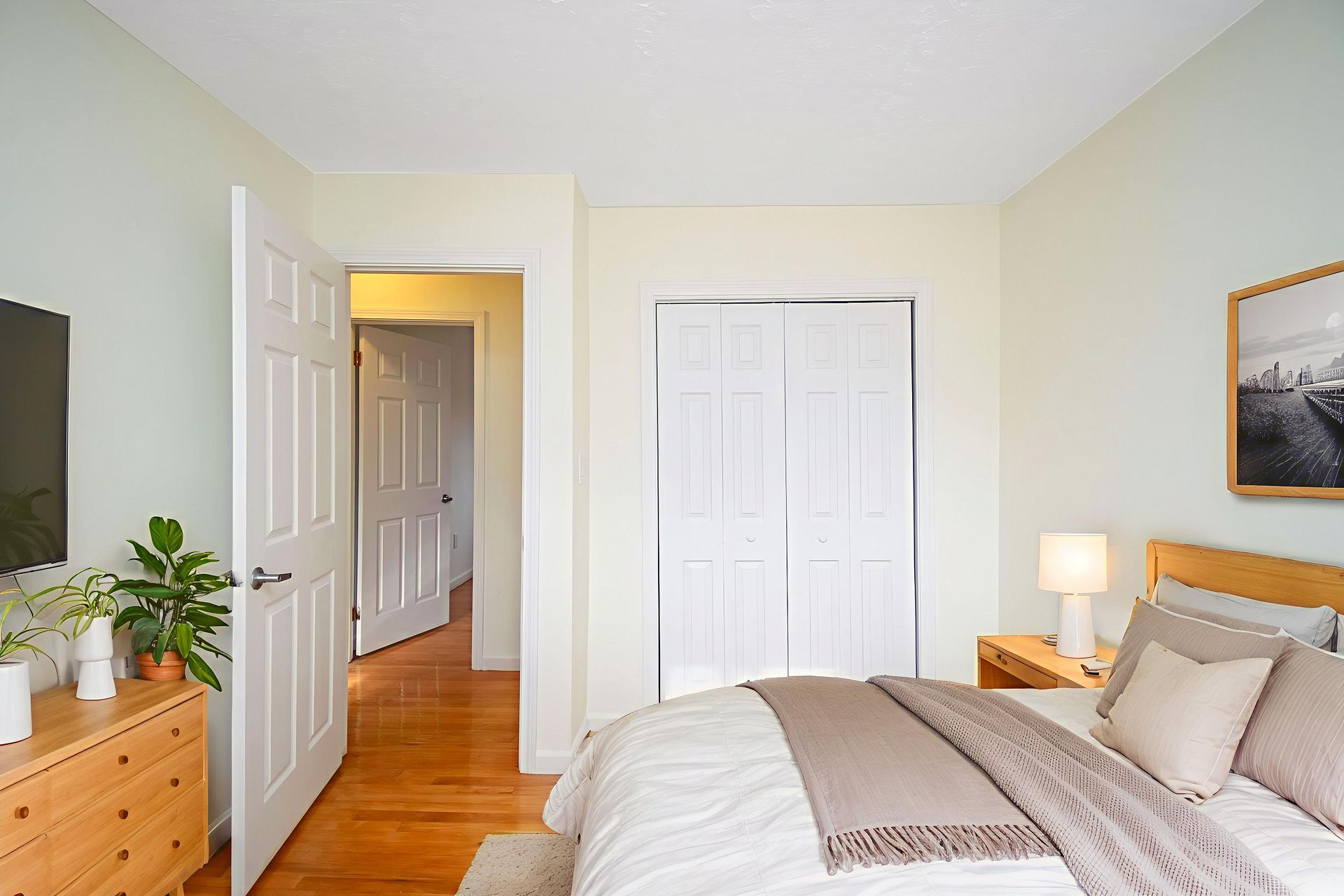 Bright bedroom with bed, dresser, open doorway, and warm wood floors