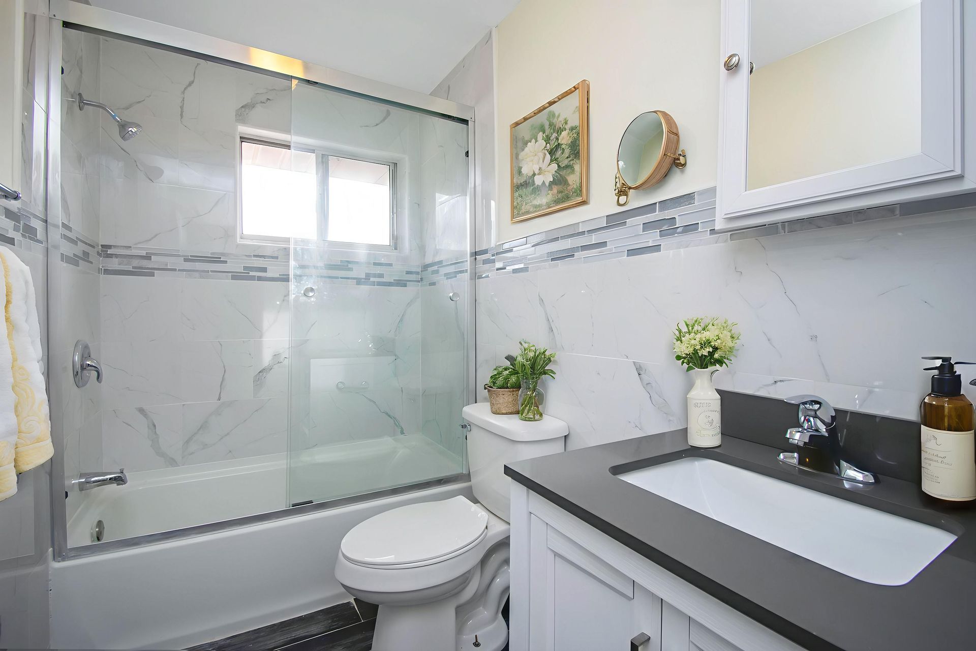 Bright modern bathroom with glass shower, white vanity, mirror, and gray countertop.