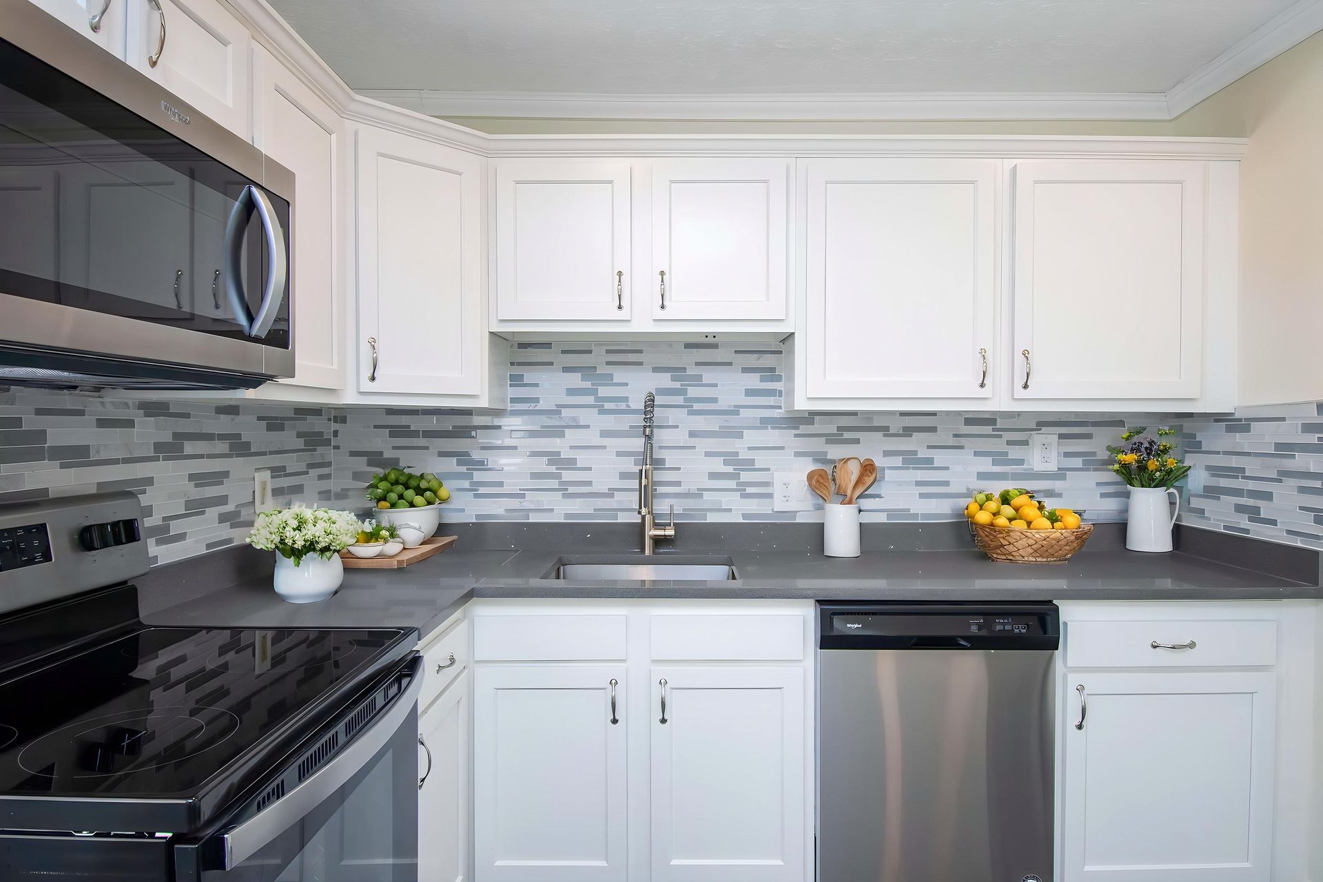 Modern white kitchen with stainless steel appliances, gray backsplash, and countertop decor