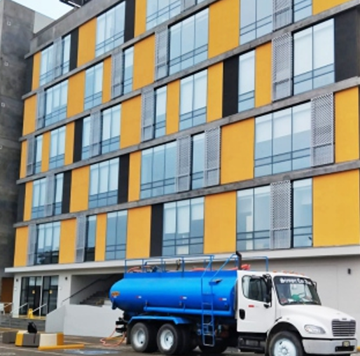 Camión blanco con cisterna azul estacionado frente a un edificio moderno con paneles amarillos y grises.