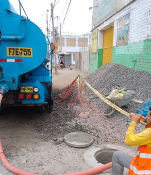 Camión azul junto a una zanja abierta con montones de grava y un trabajador con chaleco naranja supervisando las reparaciones.