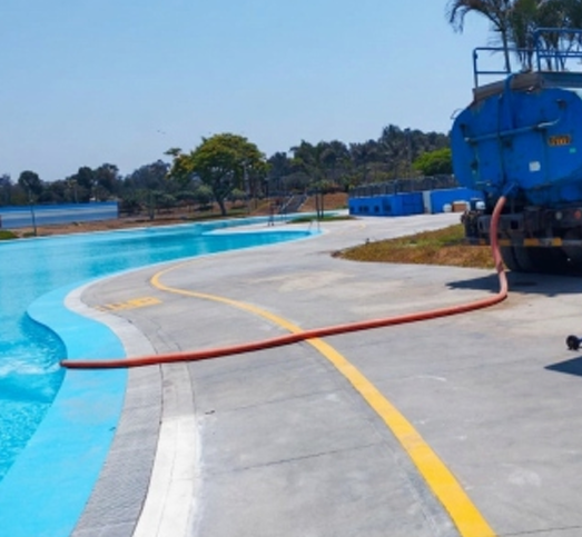 Terraza curva junto a la piscina, al lado de aguas turquesas, con un camión cisterna azul rociando agua.