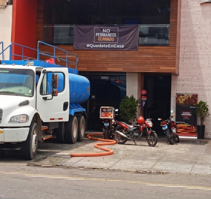 Un camión cisterna blanco estacionado frente a un edificio con motocicletas y una señal de prohibido estacionar.