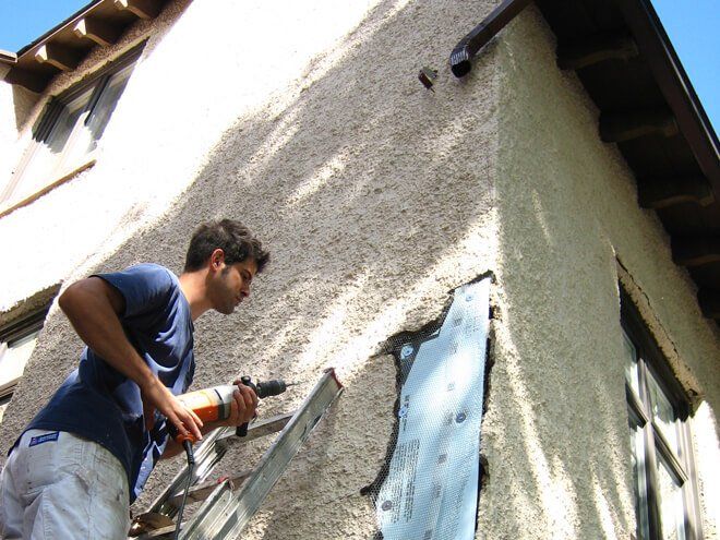 a person sealing (caulking) all the holes in a house's exterior