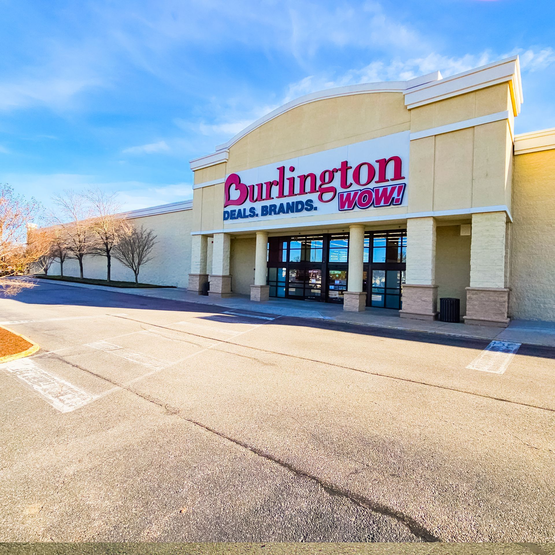 Burlington store exterior with sign: Deals, Brands, Wow! Blue sky, beige building, parking lot.