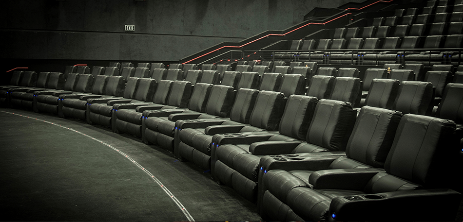 Rows of empty black theater seats in a darkened auditorium.