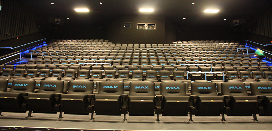 Interior view of an IMAX movie theater with rows of black seats, and a person walking in the aisle.