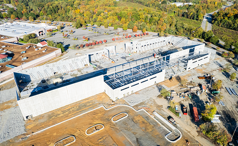 Aerial view of a large building under construction with exposed steel framework and surrounding construction materials.