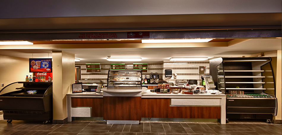 A coffee shop with a counter, display cases, and beverages.  Brown and white decor, recessed lighting.
