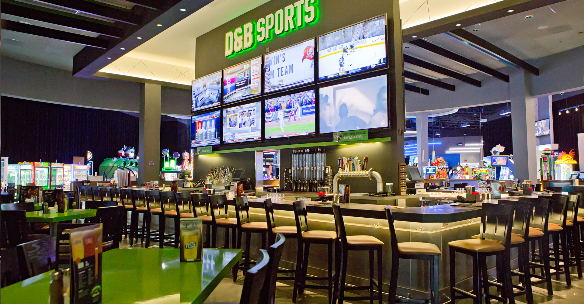 D&B Sports bar with large screens showing sports, a long bar with stools, and green tables.