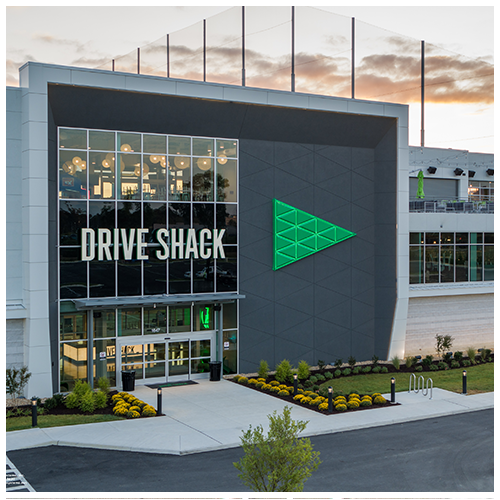 Drive Shack building exterior with glass entrance and green logo at dusk.