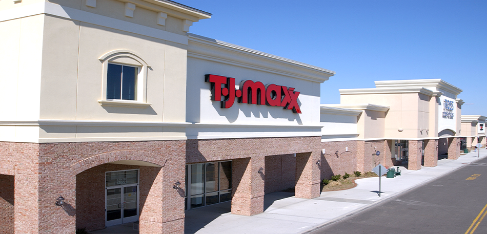 Exterior of a TJ Maxx store on a sunny day with a blue sky. The building is beige with red signage.