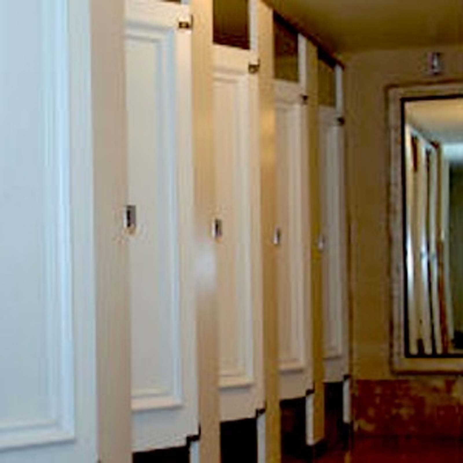 A row of white lockers in a bathroom with a mirror.