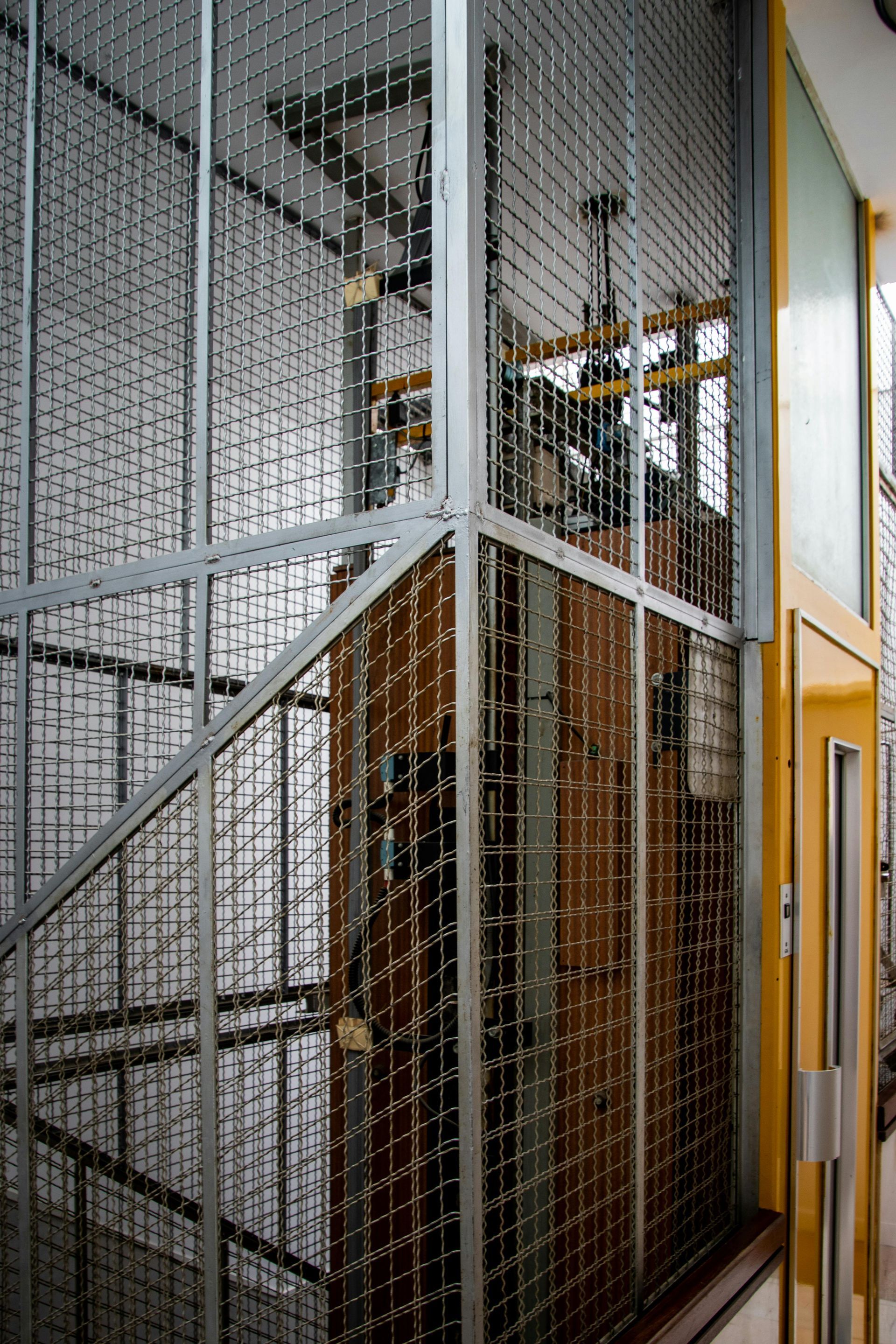 An elevator with a cage around the stairs and a yellow door.