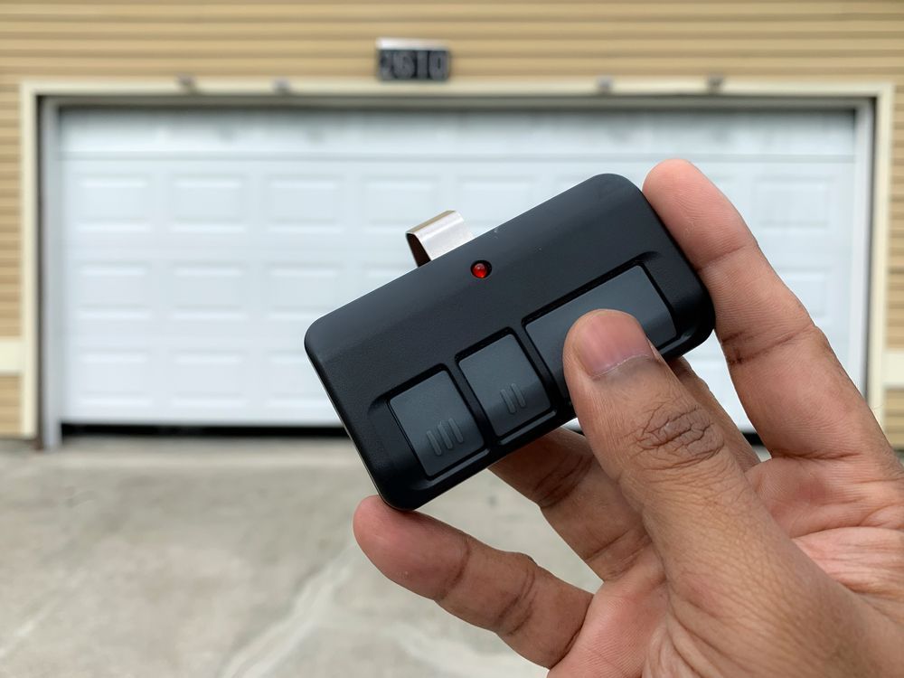 A person is holding a remote control in front of a garage door