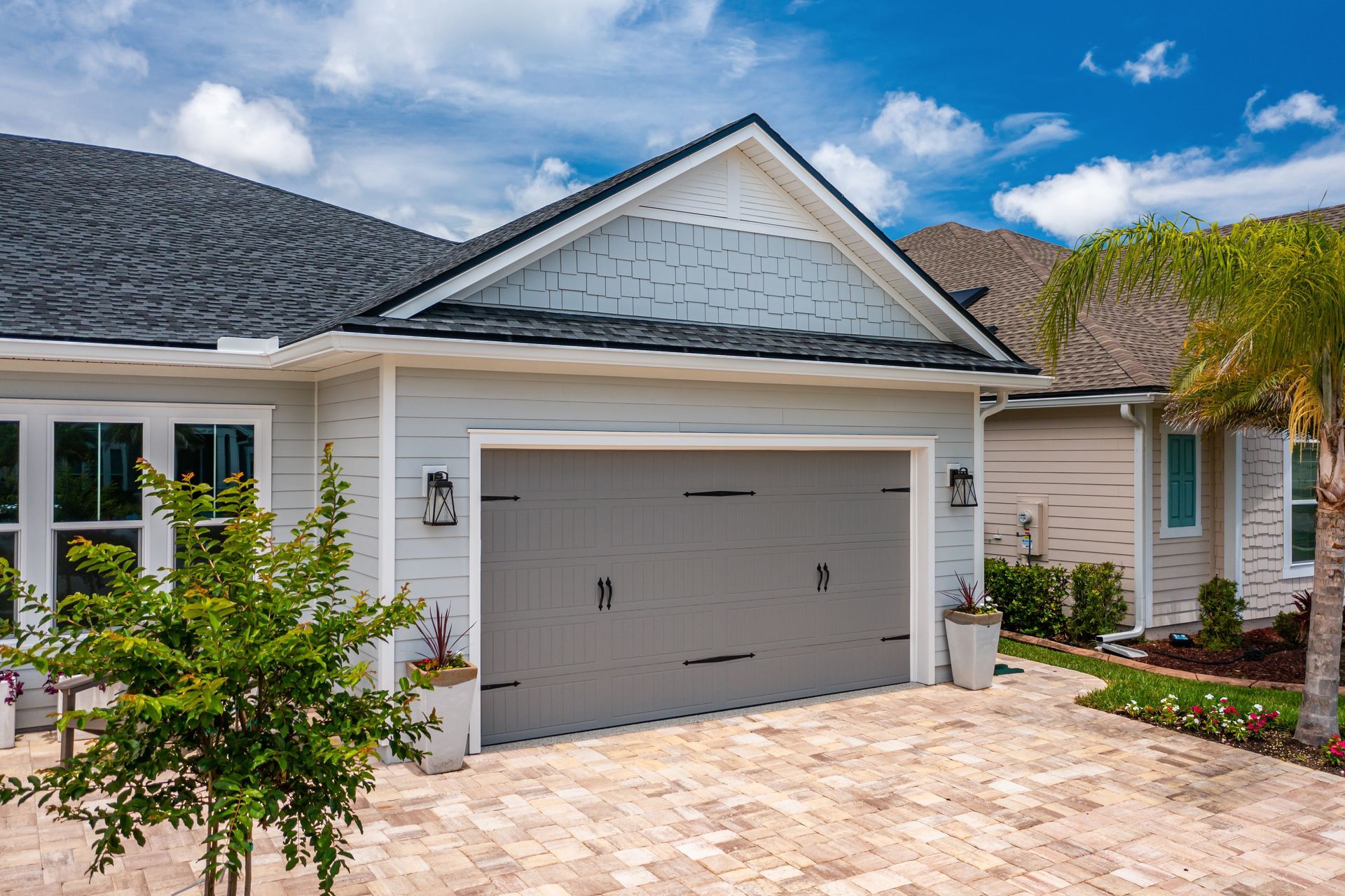 White suburban house with a gray garage door, stone driveway, and blue sky above
