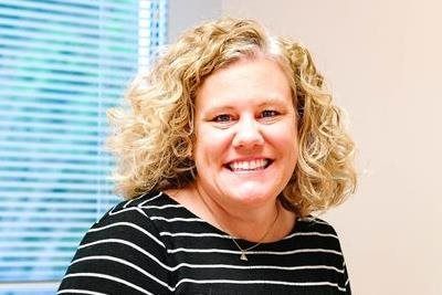 Woman with curly blonde hair smiles, wearing a striped shirt, indoors.