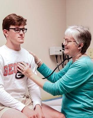 Doctor using stethoscope on a patient's chest in an exam room.