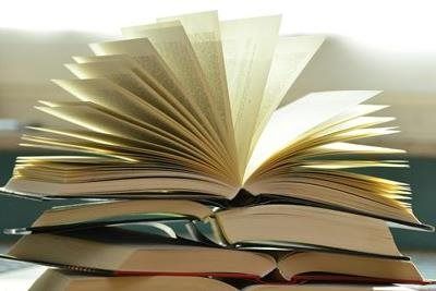 Pile of books, some open with fanned pages, against a blurred background.