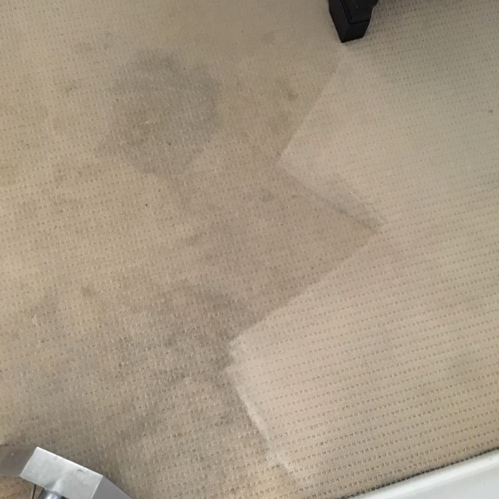 Close-up of a beige textured carpet with a darker stain and a small black furniture leg at the top. — Rudy's Carpet Cleaning & Pest Management In Sharon, QLD