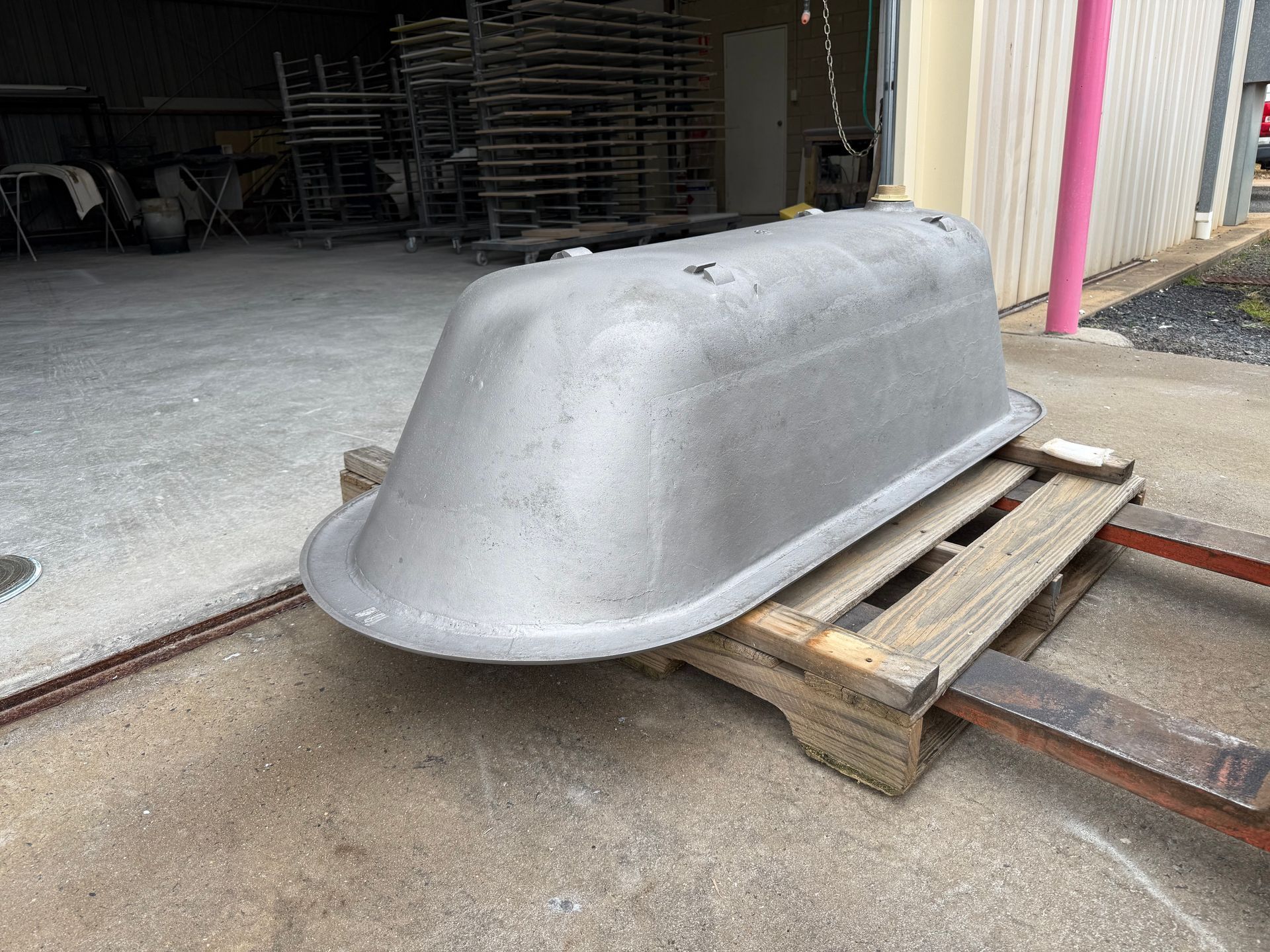 A silver bathtub on a wooden pallet outdoors in front of a building.