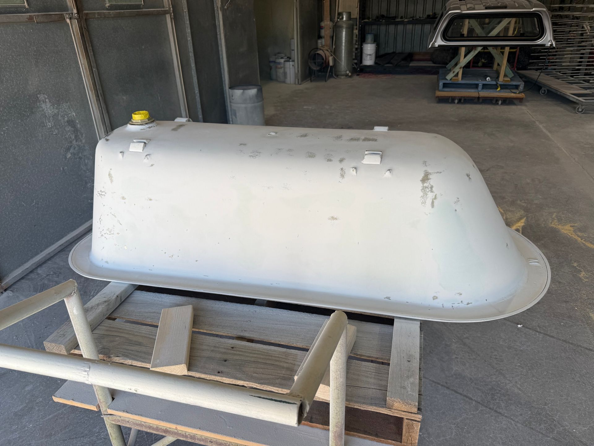 Gray bathtub, rectangular with rounded end, sits on a wooden stand outdoors, appears weathered.