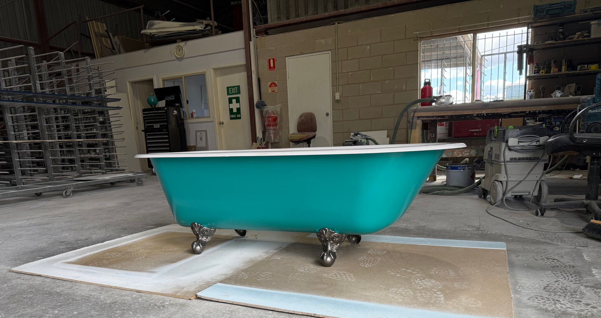 Teal claw-foot bathtub in a workshop setting, on a protective mat.