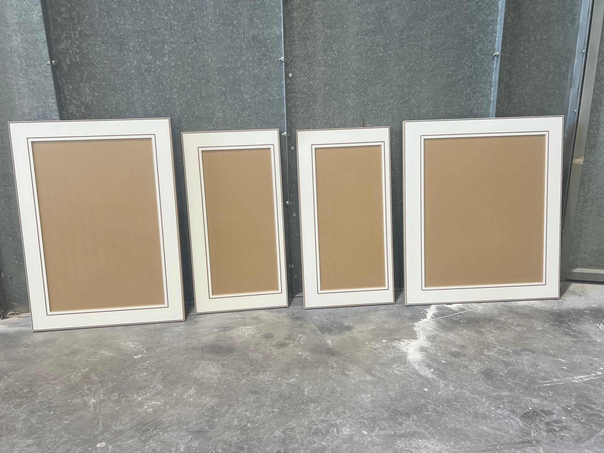 Four cream-coloured, wavy-edged picture frames of varying sizes, with brown interior panels, resting on a gray surface.