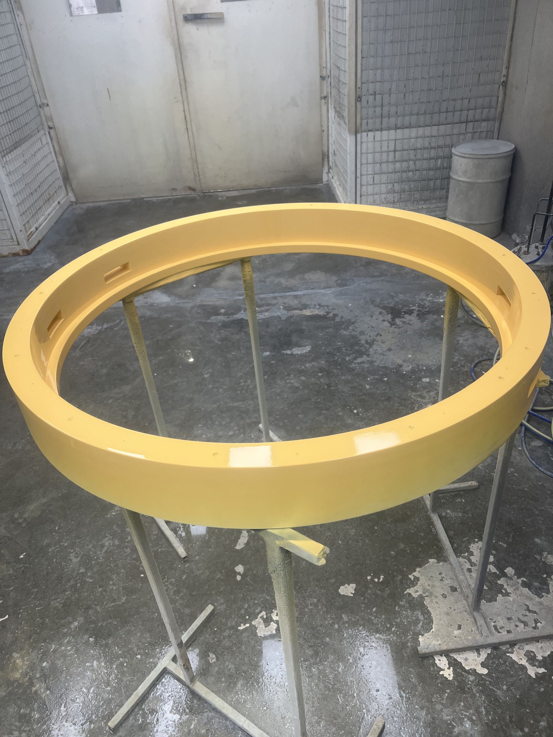 A yellow, circular frame, likely for a window or artwork, is resting on a metal stand in a workshop.