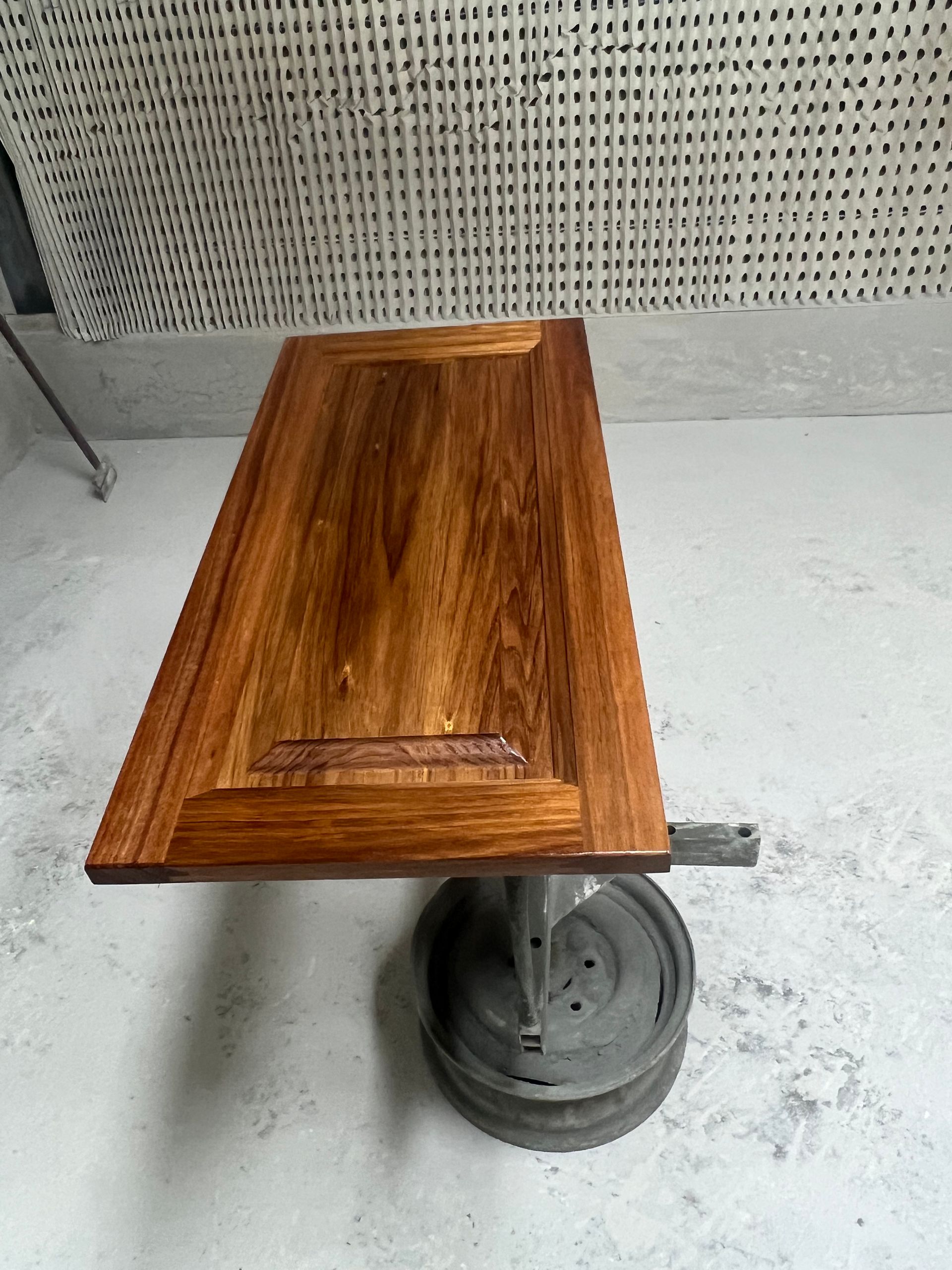 Wooden cabinet door in a workshop, finished with a brown stain, resting on a metal support.