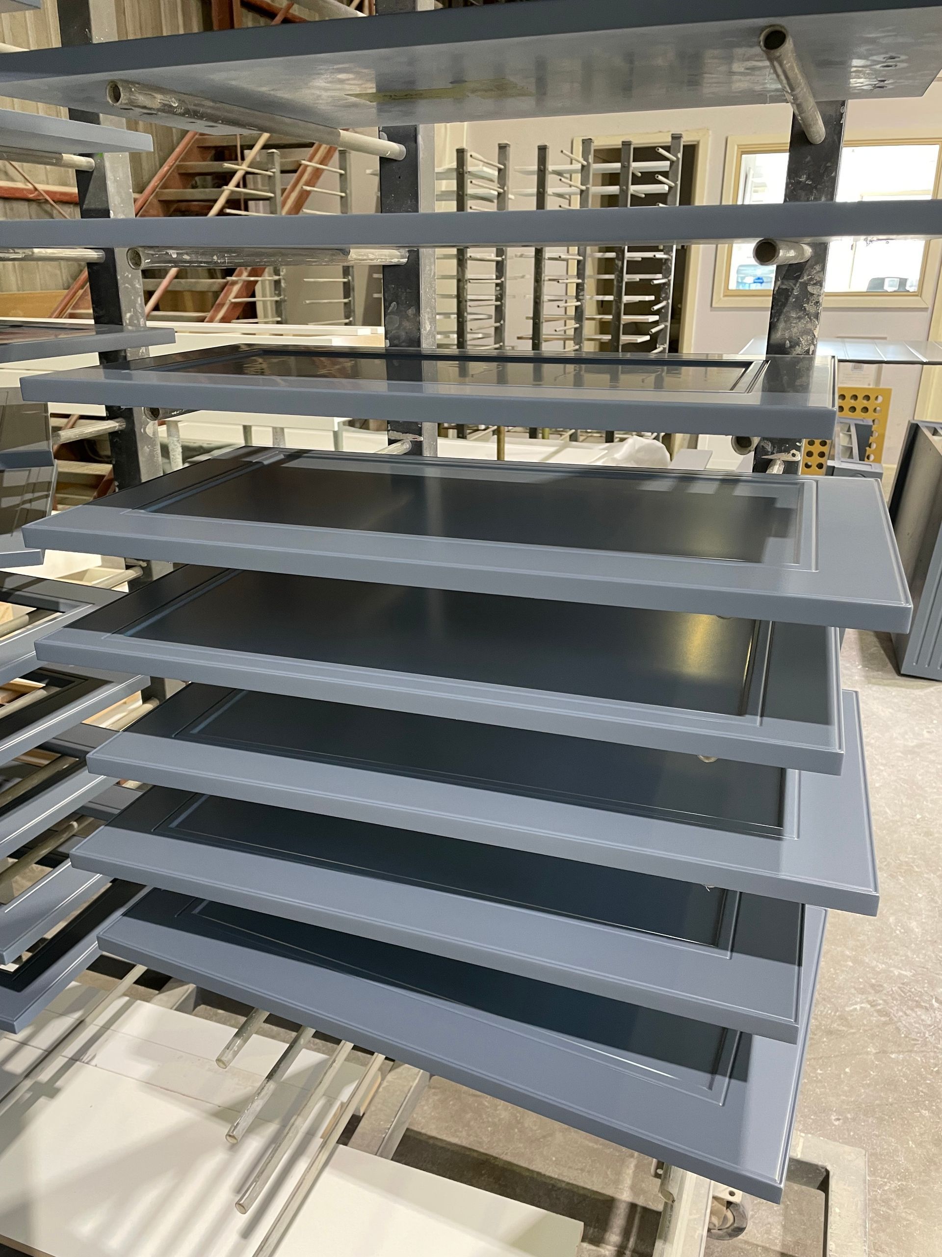 Gray painted metal cabinet doors stacked on racks in a factory.