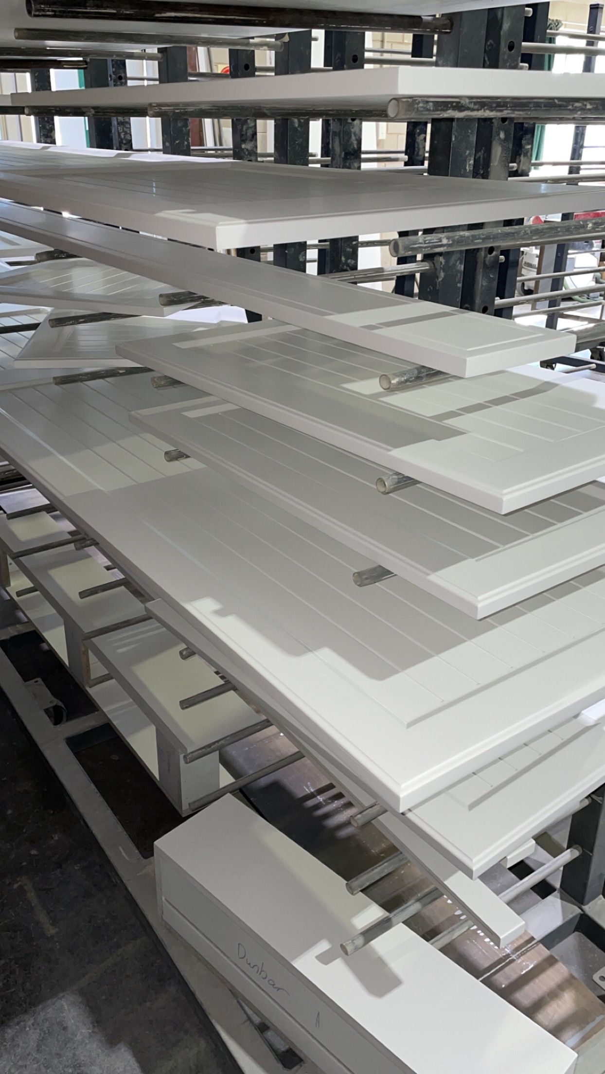 White painted doors on racks in a factory setting. Multiple layers of doors suggest production line.
