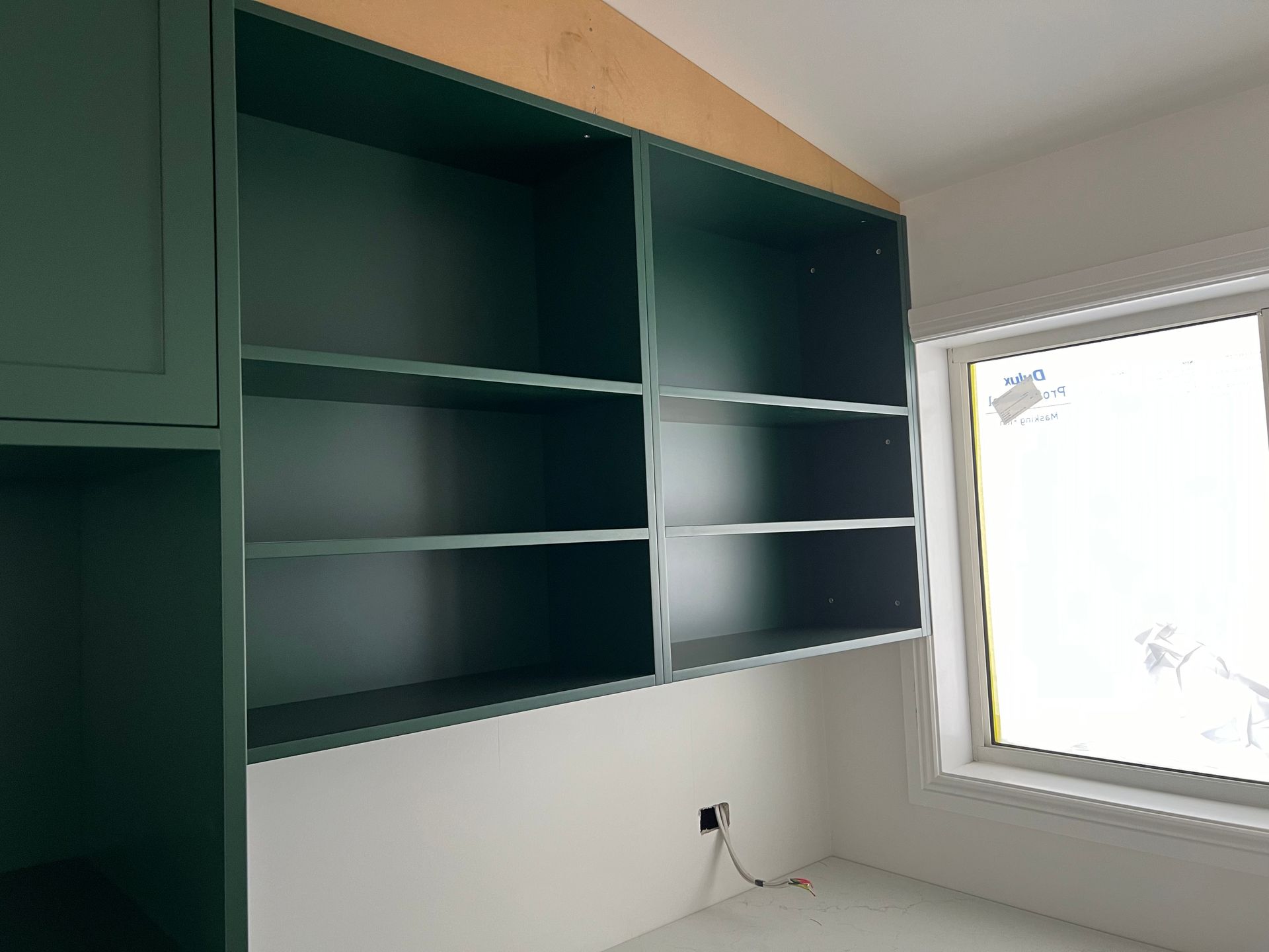 Green built-in shelves above a white wall. A window is on the right, and a cabinet is on the left.